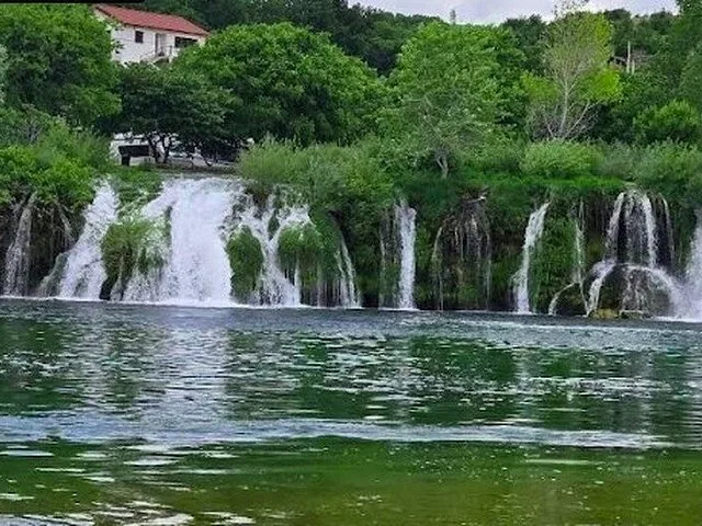 Scenic view of a wide, low waterfall cascading into a green, tranquil river.