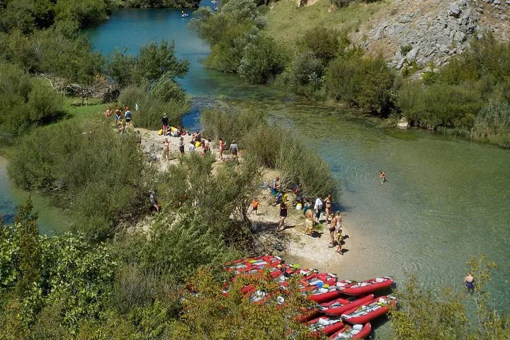 Des personnes se rassemblent sur une berge sablonneuse, avec de nombreux kayaks rouges à proximité.