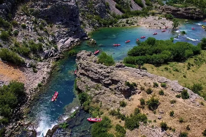 Red kayaks navigate a winding, clear river flowing through a rocky, green canyon.