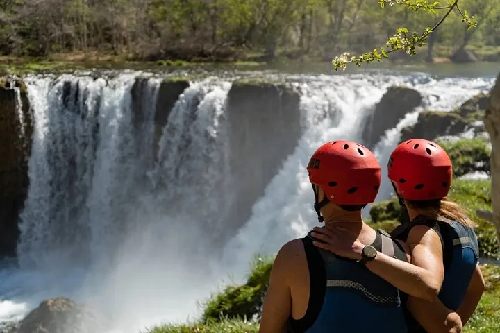 Deux personnes portant des casques rouges et des gilets de sauvetage contemplent une cascade.