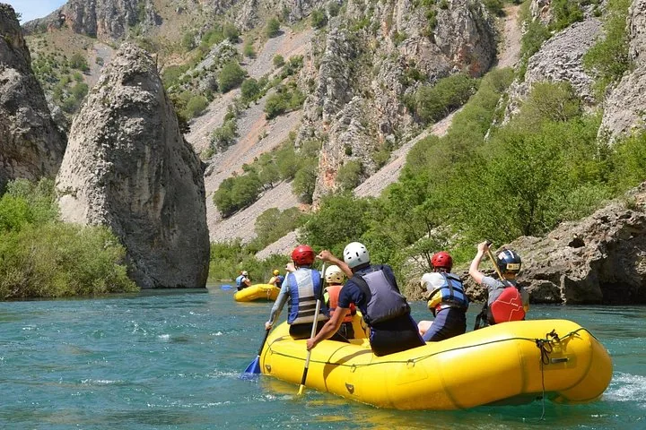 Ein gelbes Raft voller Menschen bewegt sich auf ruhigem türkisfarbenem Wasser nahe hoher Felskliffe.