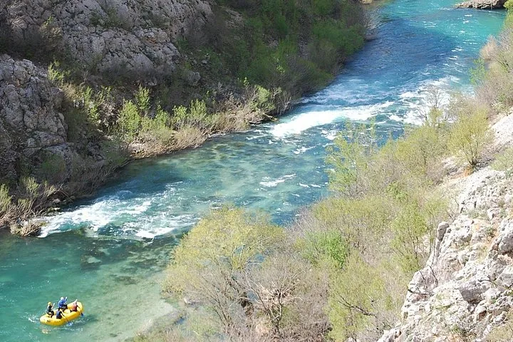 Un radeau jaune descend une rivière claire et étroite qui serpente à travers des falaises rocheuses et escarpées.